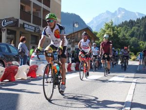 Cyclists riding through a village with mountains